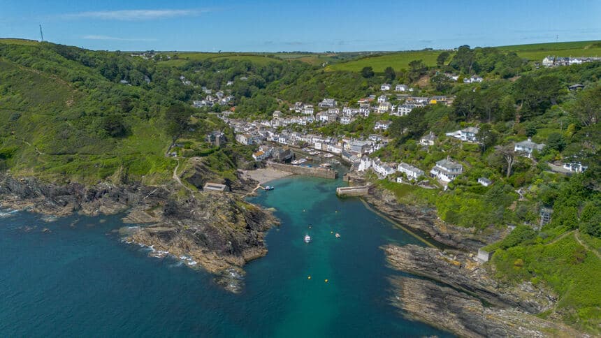 Aerial view of a Cornish harbour village with turquoise water and white cottages on green hillsides