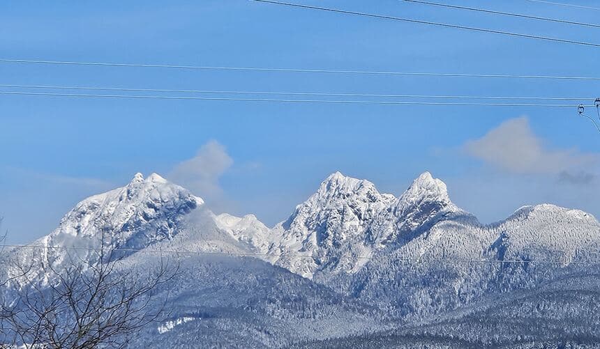 Snow-covered mountain peaks under a blue sky, with power lines crossing the entire frame